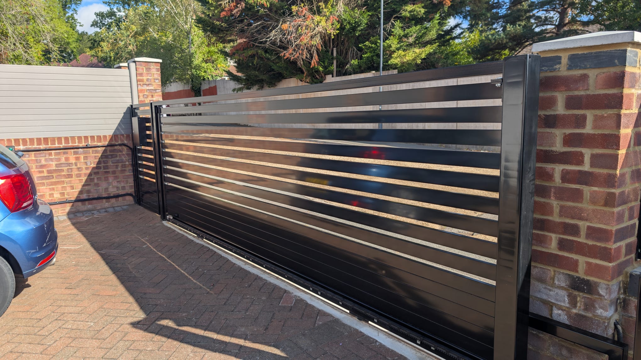 Automated sliding driveway gate installed between brick piers, with a car parked behind it
